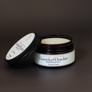 A jar of Gornik & Drucker barbering textured paste with the lid off, displayed on a dark background.