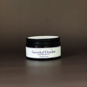 A jar of texture paste for hair styling, with a label that includes the brand name and product title.