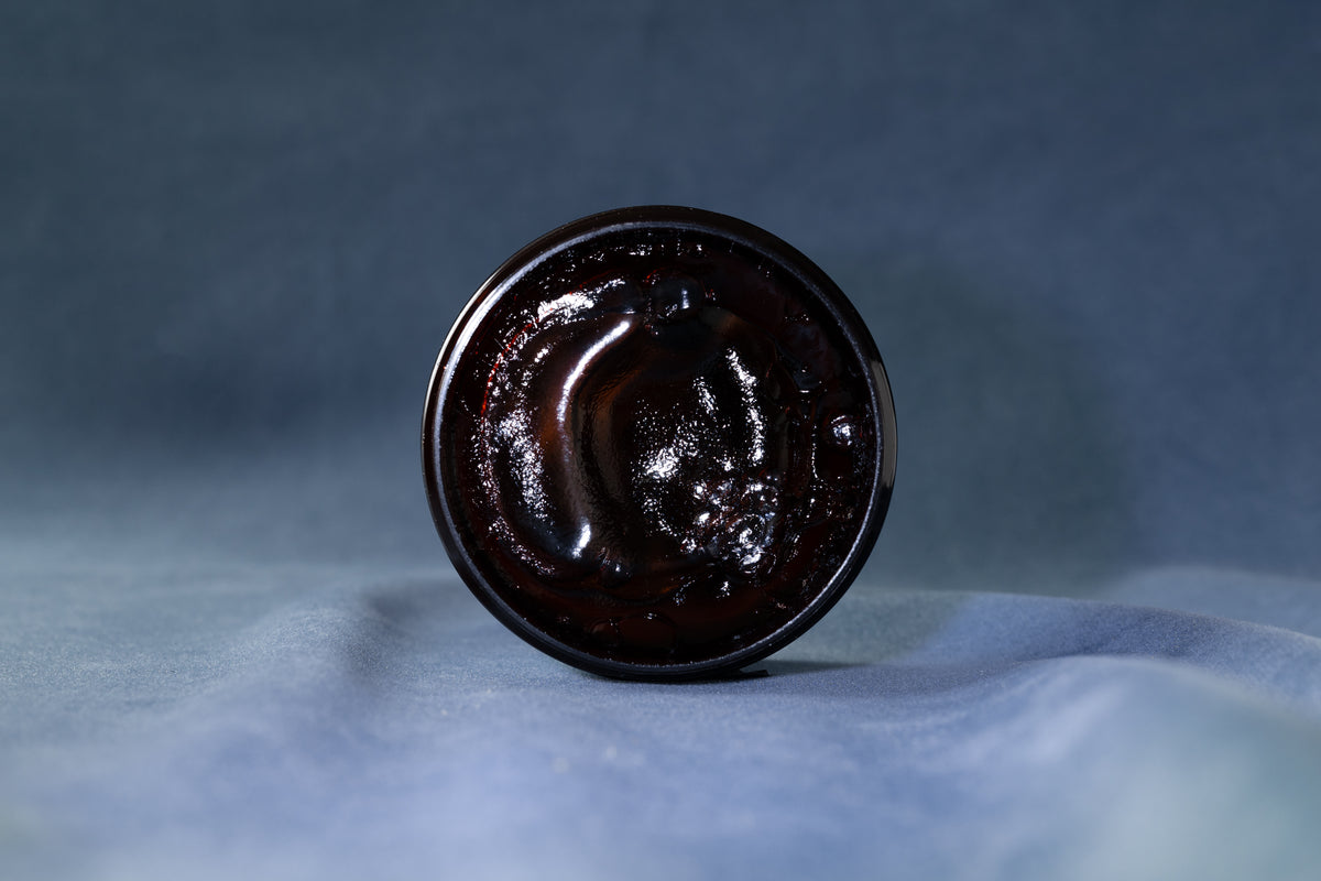 The rich dark texture of Deluxe Pomade in the open jar
